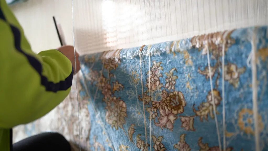 Artisan weaving a handmade silk rug on a vertical loom