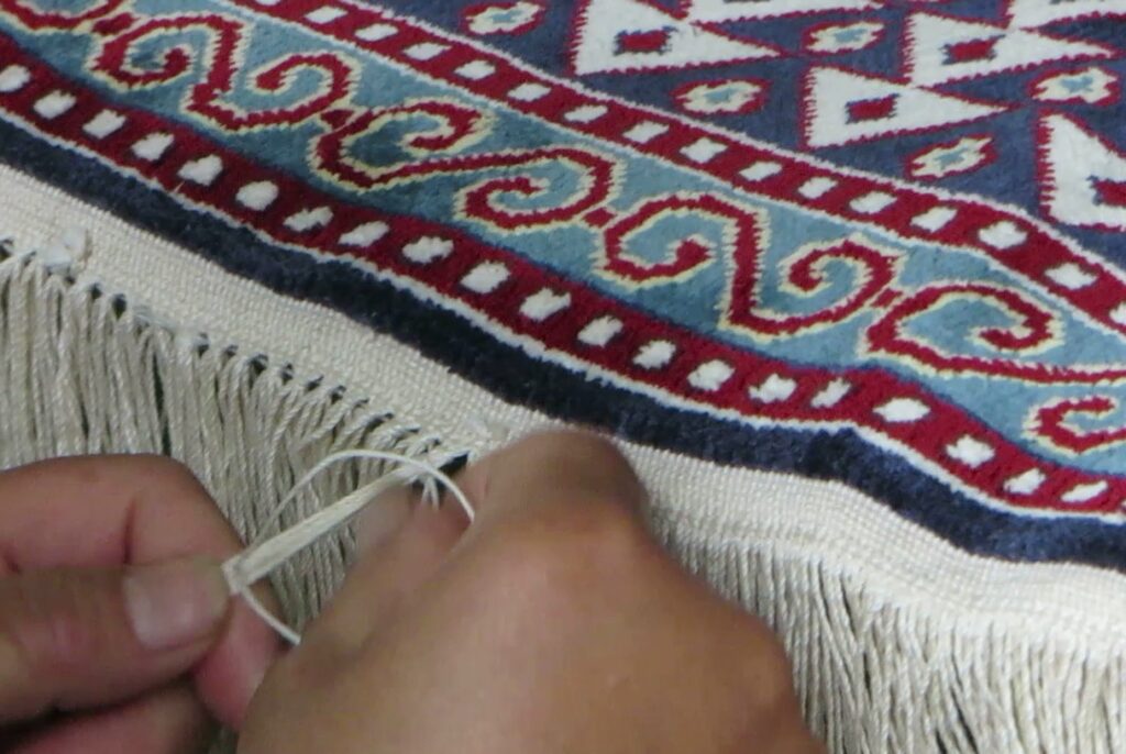 Fringes of a handmade silk rug being finished by hand