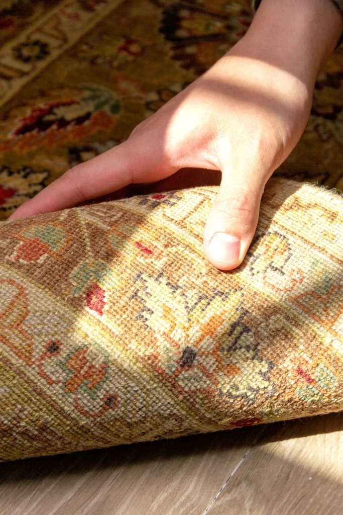 | A hand lifting a patterned rug to show its reverse and edge