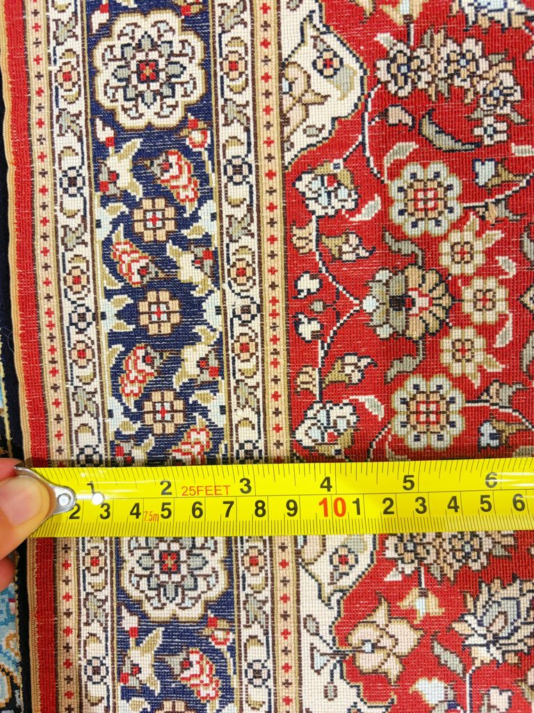 Fine floral and border details on a hand-knotted silk rug shown beside a ruler